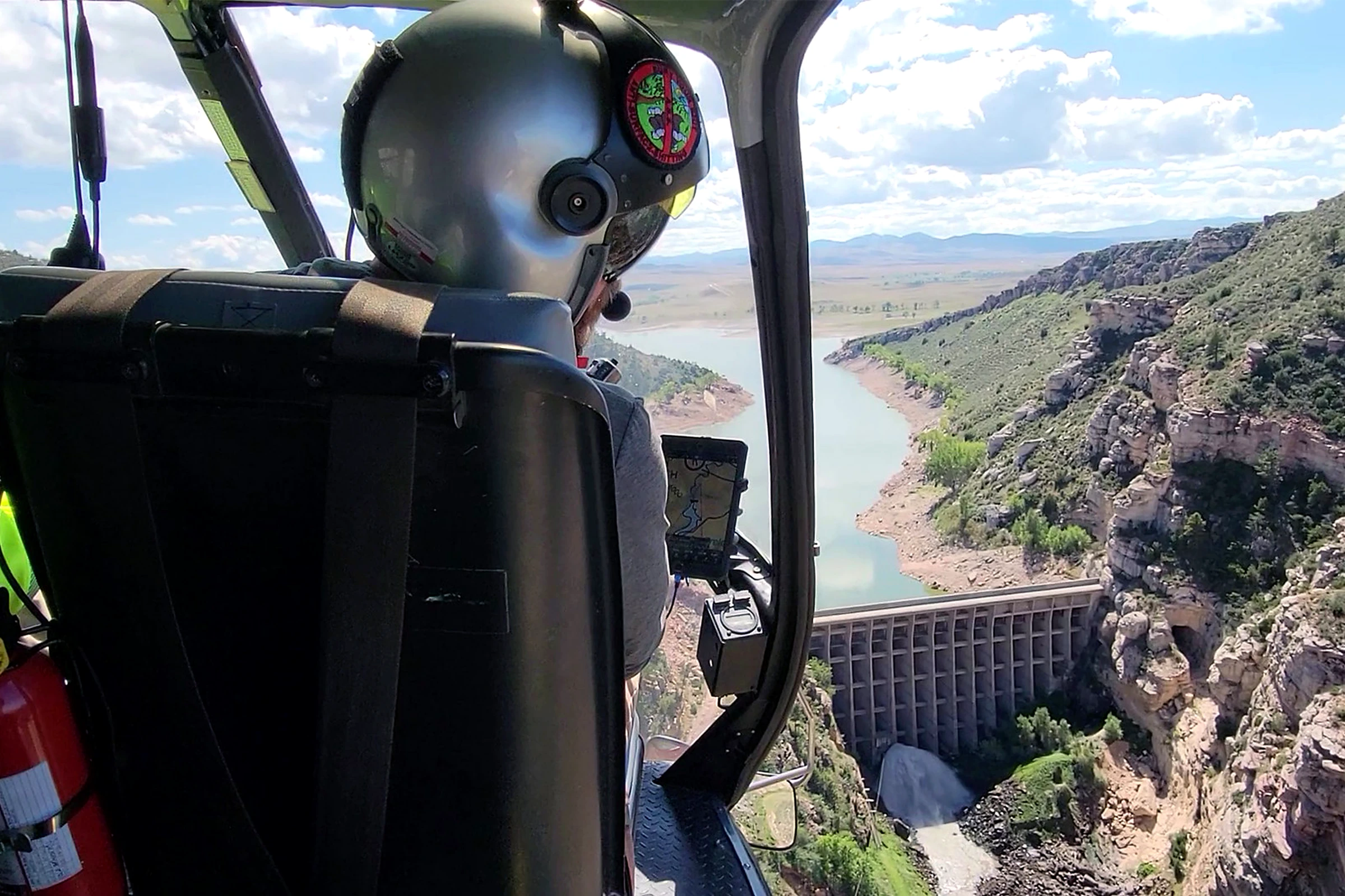 View from a helicopter cockpit over a dam and canyon